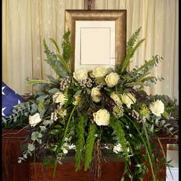White rose funeral spray with cascading greenery in front of a framed display