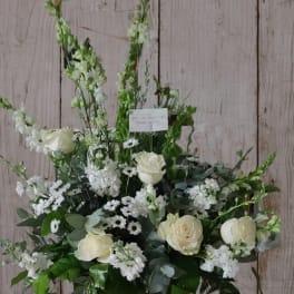 White floral arrangement with roses and tall snapdragons in a bronze vase