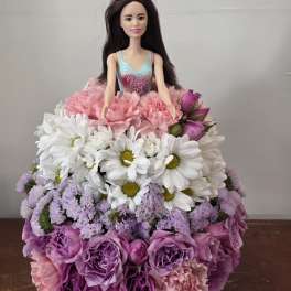 Doll in a dress surrounded by a pink, white, and purple flower arrangement