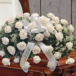 White rose casket spray with satin ribbon on a wooden casket