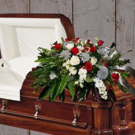 Casket spray of red and white roses with greenery on a wooden casket