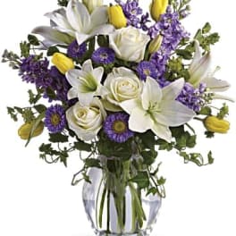 Bouquet of white lilies, roses, and purple flowers in a glass vase