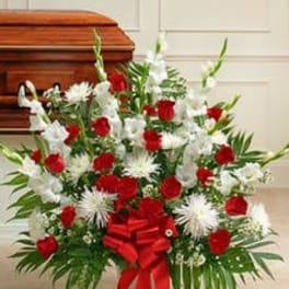 Large red and white sympathy arrangement with bow displayed in front of a wooden casket