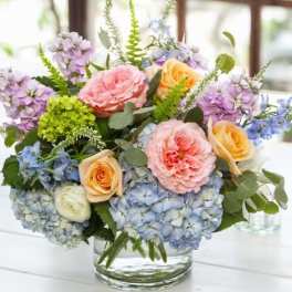 Pastel bouquet of roses, hydrangeas, and purple blooms in a glass vase
