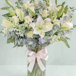 White lilies and roses in a glass vase with a pale ribbon