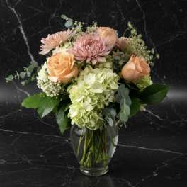 Peach roses and pink blooms in a clear glass vase