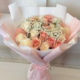 Bouquet of pink and cream roses with baby's breath in pink wrapping