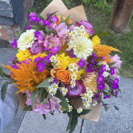 Mixed bouquet with roses, daisies, and bright orange accents in brown paper