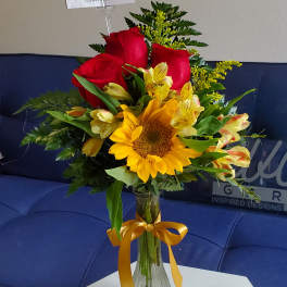 Bouquet of red roses and yellow flowers in a glass vase with a ribbon