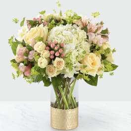 Bouquet of cream and pink flowers in a clear vase with a gold wrap