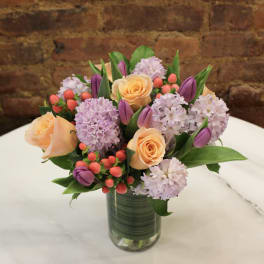 Bouquet of peach roses, lavender blooms, and purple tulips in a glass vase