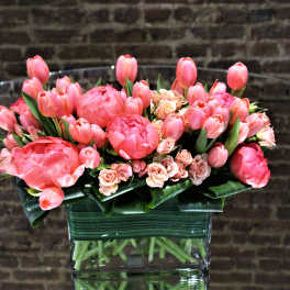 Pink tulips and small roses arranged in a clear glass vase