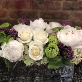 White roses and peonies with green and purple accents in a low arrangement