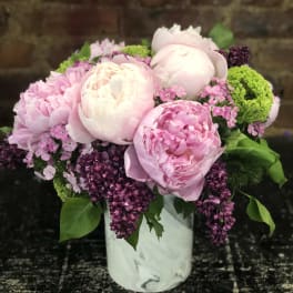 Pink peonies and purple blooms arranged in a white vase
