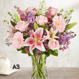 Pink roses and lilies arranged with gerberas in a clear glass vase
