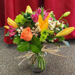 Mixed bouquet of lilies, roses, and small white flowers in a glass vase