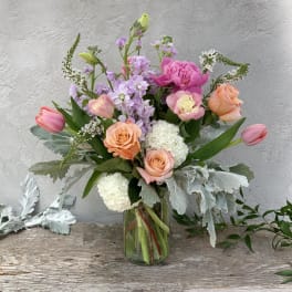 Mixed bouquet of pink, peach, and lavender flowers in a glass vase