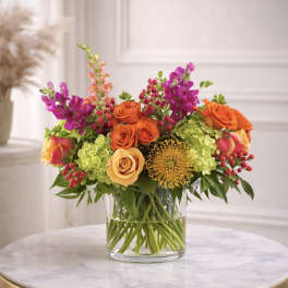 Bright arrangement of orange roses, green hydrangeas, and pink snapdragons in a clear glass vase