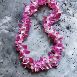 Purple and white orchid flower lei arranged in an oval on a gray stone surface