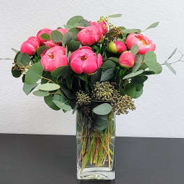 Pink peonies arranged in a clear glass vase with round eucalyptus leaves.