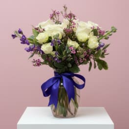 White and purple flower bouquet in a glass vase with a blue ribbon