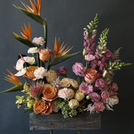 Tall floral arrangement with orange birds of paradise and pink roses in a wooden container
