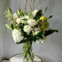 Tall arrangement of white roses, lilies, hydrangeas, and green orchids in a clear glass vase
