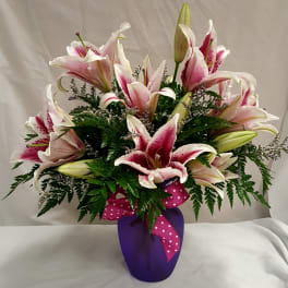 Pink and white lilies arranged in a purple vase with a polka-dot ribbon
