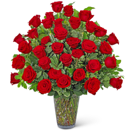 Red roses arranged in a clear glass vase with green foliage