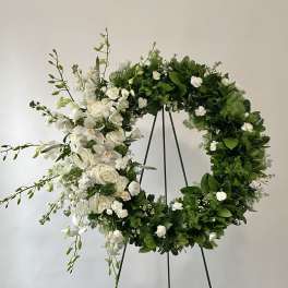 White floral wreath on a black stand with trailing blooms