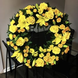 Yellow floral wreath with roses, lilies, and daisies on a stand