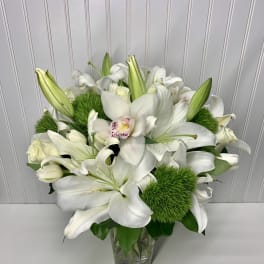 White lilies and orchids arranged in a clear glass vase