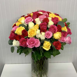 Tall clear vase filled with a large, dome-shaped arrangement of red, pink, yellow and white roses.