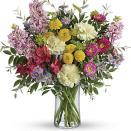 Mixed bouquet of pink, yellow, purple, and white flowers in a glass vase