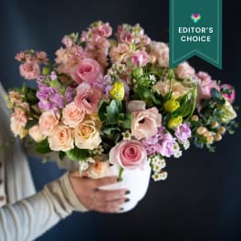 Handheld bouquet of pink and peach flowers in a white vase