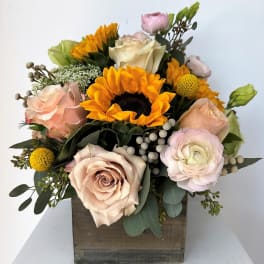 Mixed bouquet with sunflowers, roses, and pale pink blooms in a wooden box