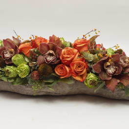 Low floral arrangement with orange roses and burgundy orchids in a rustic wood container