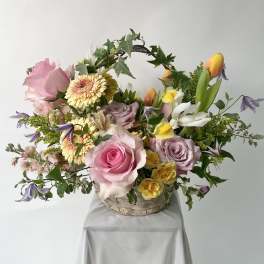 Pastel basket arrangement with pink roses, yellow gerberas, tulips, and an ivy-wrapped handle.