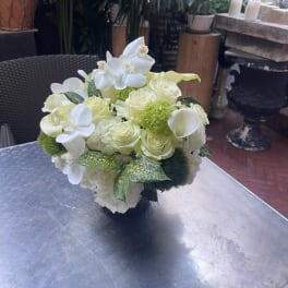White floral arrangement with roses, orchids, and calla lilies in a dark vase