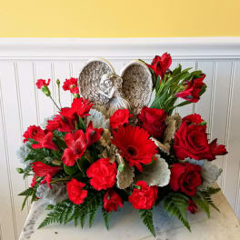 Red floral arrangement with roses, gerbera daisies, and carnations around an angel wing ornament
