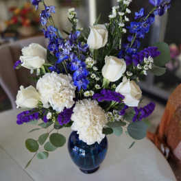 White roses and carnations with blue delphinium in a blue vase