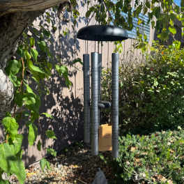 Black memorial wind chime hanging outdoors among trees and shrubs