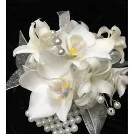 White orchid wrist corsage with silver ribbon and pearl accents on a black background