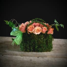 Peach roses arranged in a moss-covered basket with trailing ivy