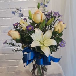 Bouquet of white lilies, cream roses, and purple flowers in a glass vase