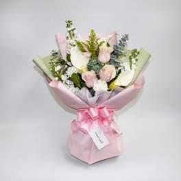 Bouquet of pale pink and white flowers wrapped in pink paper with a ribbon