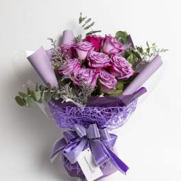 Bouquet of purple roses wrapped in lavender paper with a ribbon