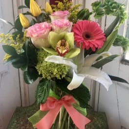 Mixed bouquet in a glass vase with pink roses, yellow tulips, and a pink gerbera daisy