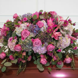 Large pink and lavender floral arrangement on a wooden casket