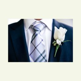 White boutonniere pinned to a dark suit jacket beside a plaid tie